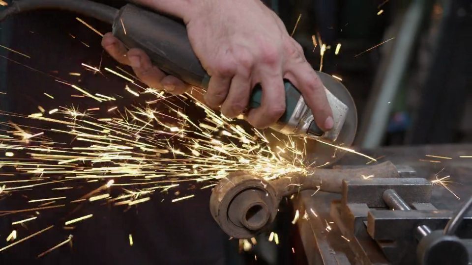 Angle grinder cutting steel pipe stock, sparks flying